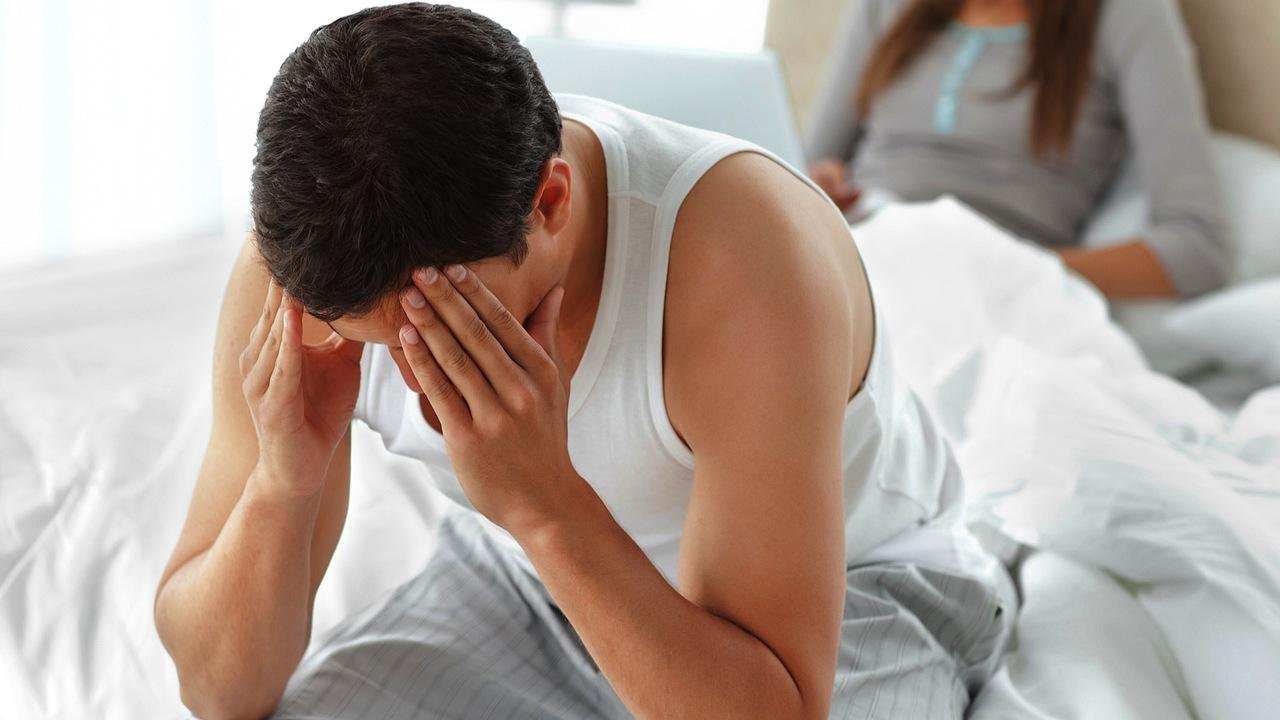 Homem sentado na cama, com as mãos no rosto