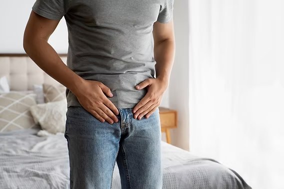 Homem em pé, com a mão sobre a região inguinal